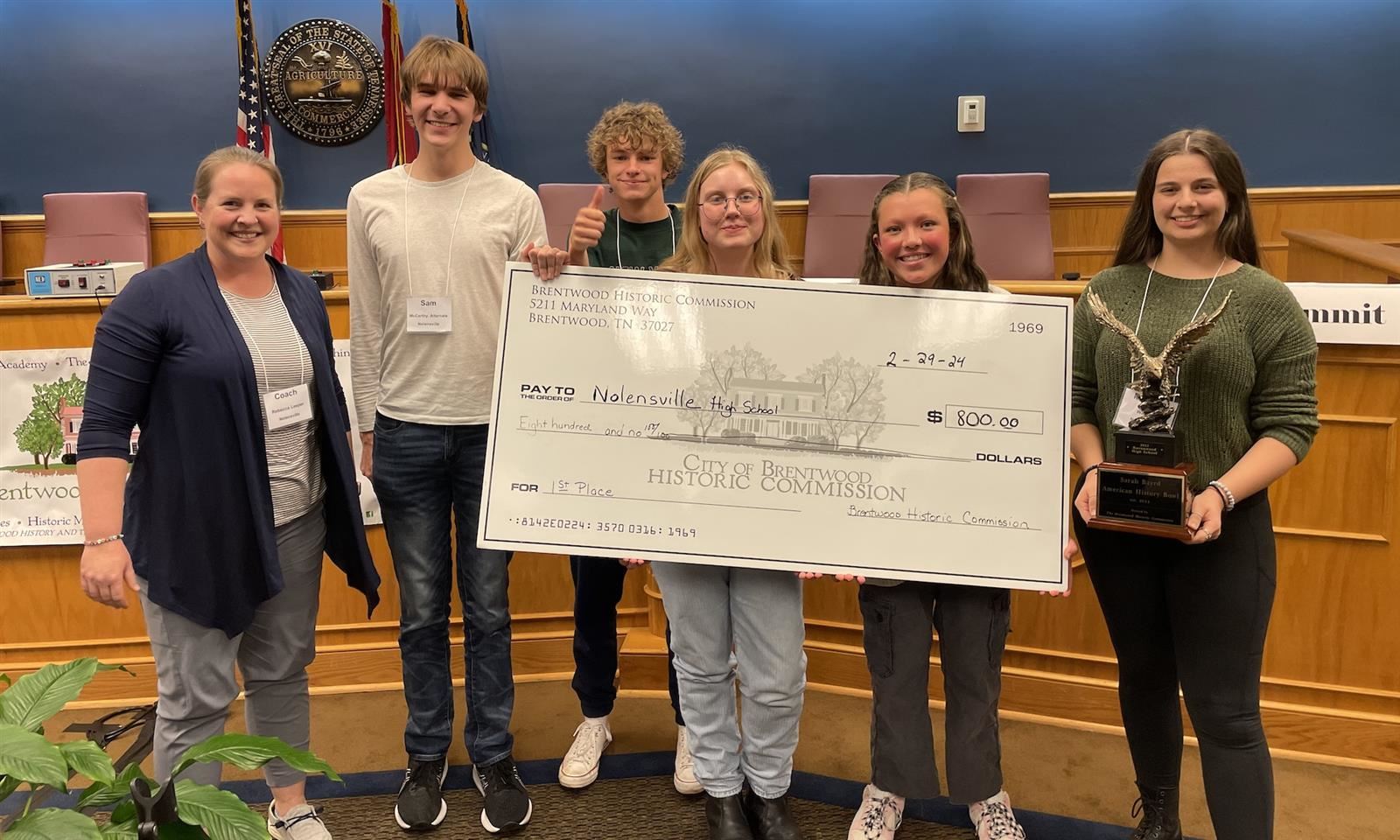 Students smile while holding a large cardboard check